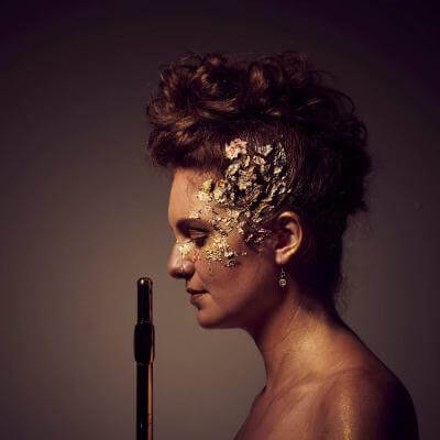 Photo of Ariane Brisson in profile with makeup, hoding her flute